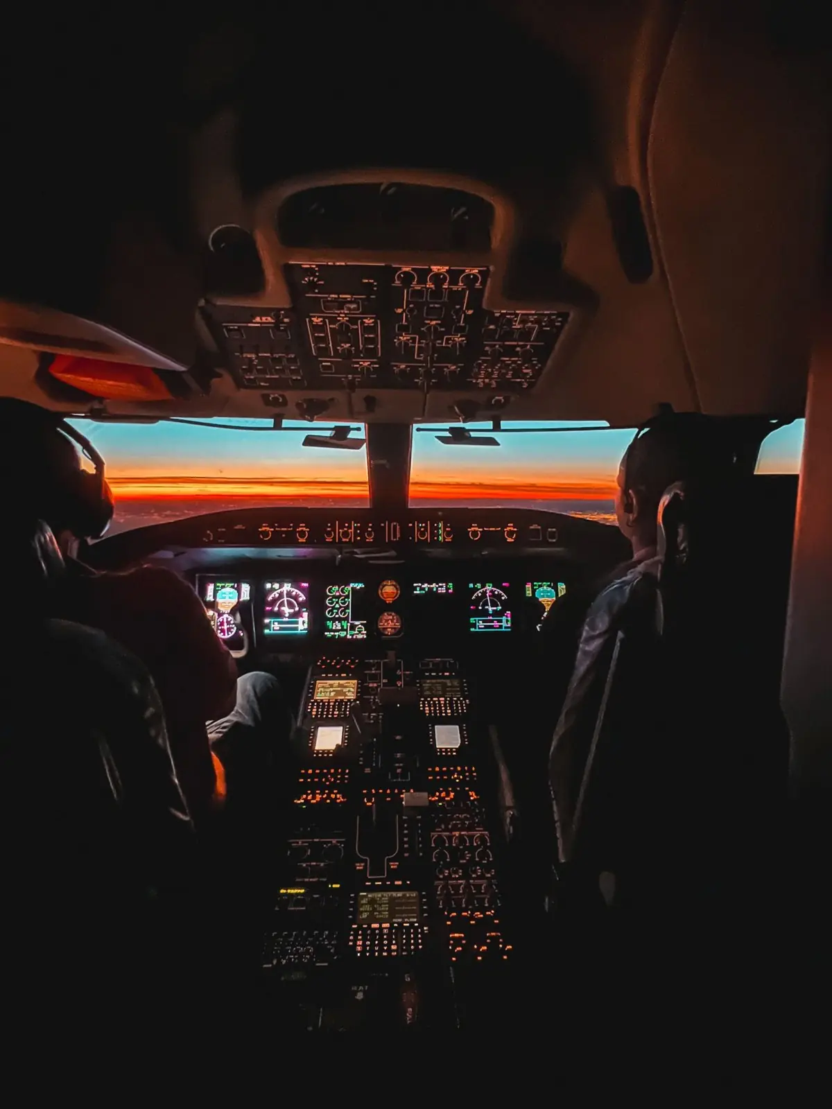 Two pilots on the flight deck at sunset, instruments glowing